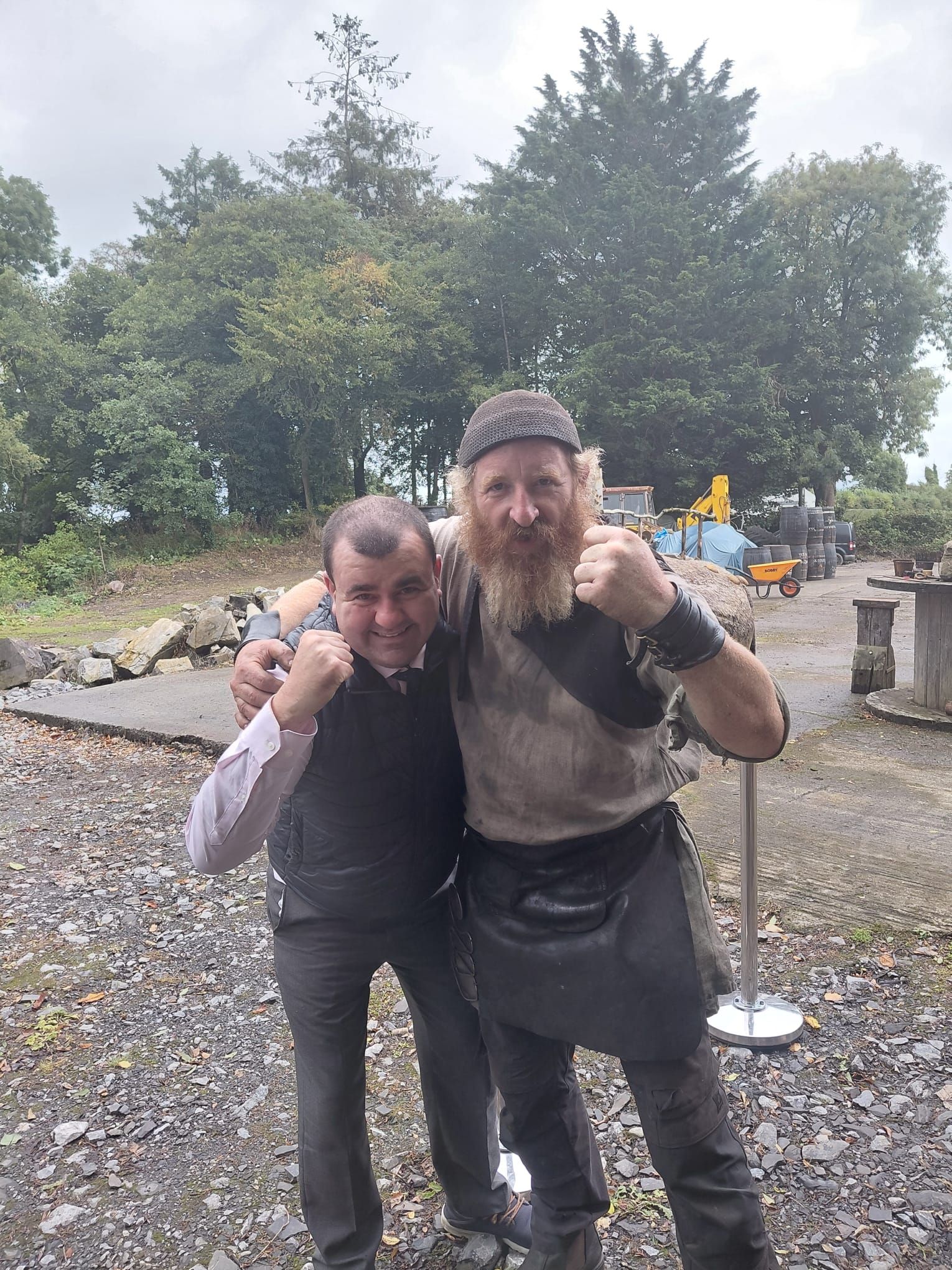 The chauffeur and a bearded craftsman in a work apron raise their fists and grin for the camera.