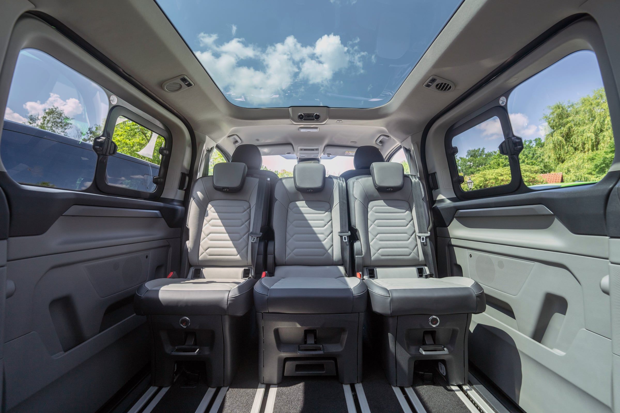 The rear cabin of a Ford Tourneo Custom, with grey leather seats under a glass roof.