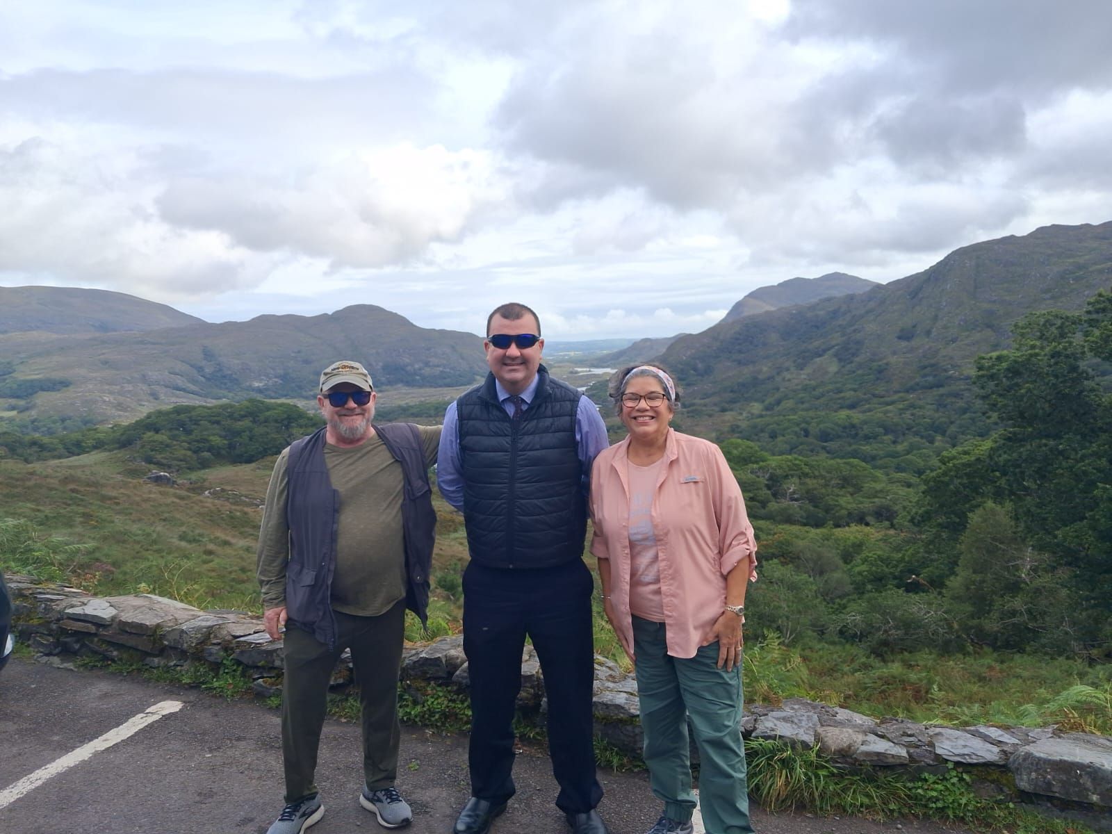 Paul, in sunglasses, stands between two guests at a viewpoint over a wide valley and mountains.